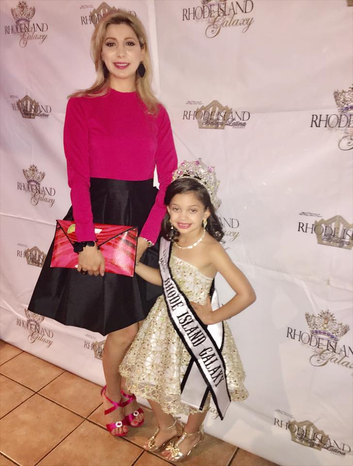 Chirin Ashkar wearing a black Lalla Bee skirt with a red top and statement clutch at the Rhode Island Galaxy Pageant, standing beside a young pageant winner.