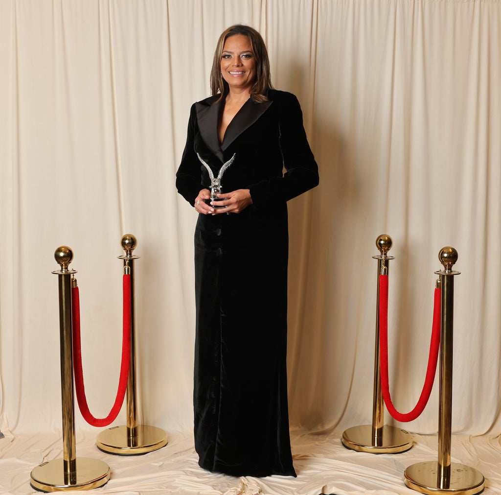 Melina Cortes-Nmili wins the 2025 Eagle Award in a stunning black velvet tuxedo dress with mikado collar, celebrating her vision and leadership in fashion.