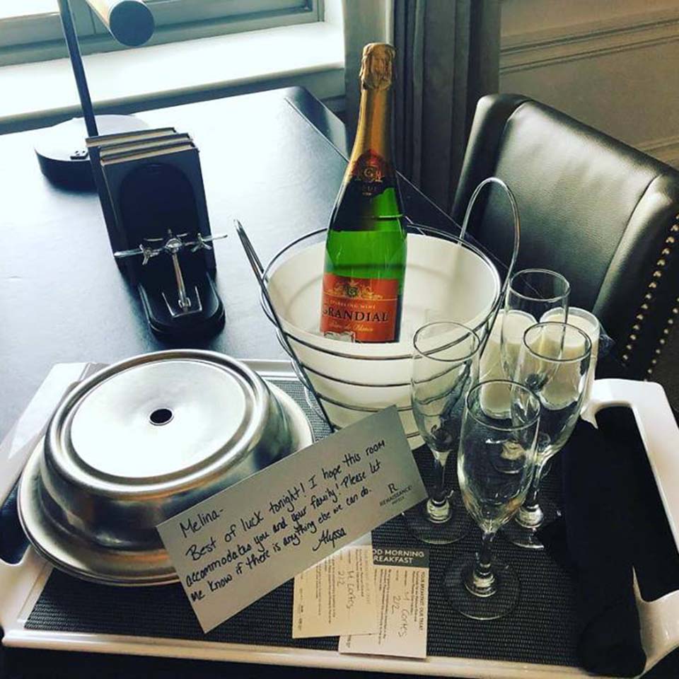 Champagne bottle in ice bucket with glasses and handwritten note on hotel tray symbolizing gratitude and support.