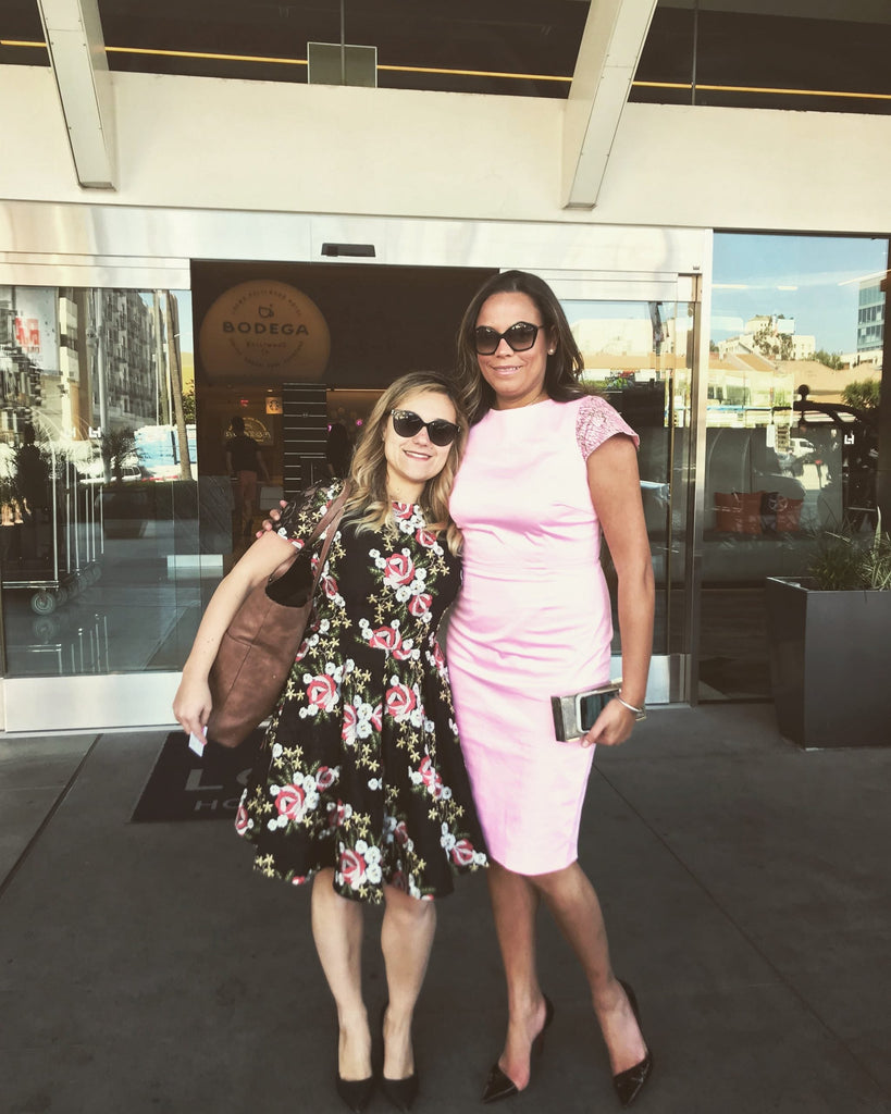 Melin and Jackie posing outside in Los Angeles, one wearing a black floral Lalla Bee dress and the other in a pink fitted dress.