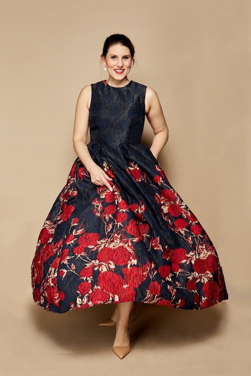Andrea Poisson DeLucia wearing a navy Lalla Bee ball gown with red floral embroidery, posing against a beige background.