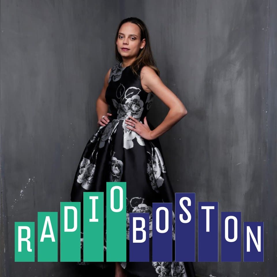 Fashion designer Melina Cortes-Nmili wearing a black floral gown, featured by Radio Boston in coverage of Boston Fashion Week’s 25th anniversary.