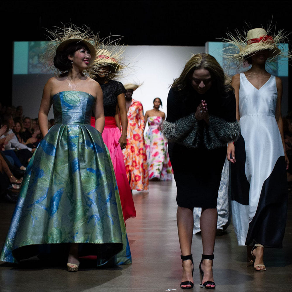 Melina Cortes-Nmili bowing on the runway alongside models wearing vibrant gowns and wide-brimmed hats from the Island Dreams Collection.