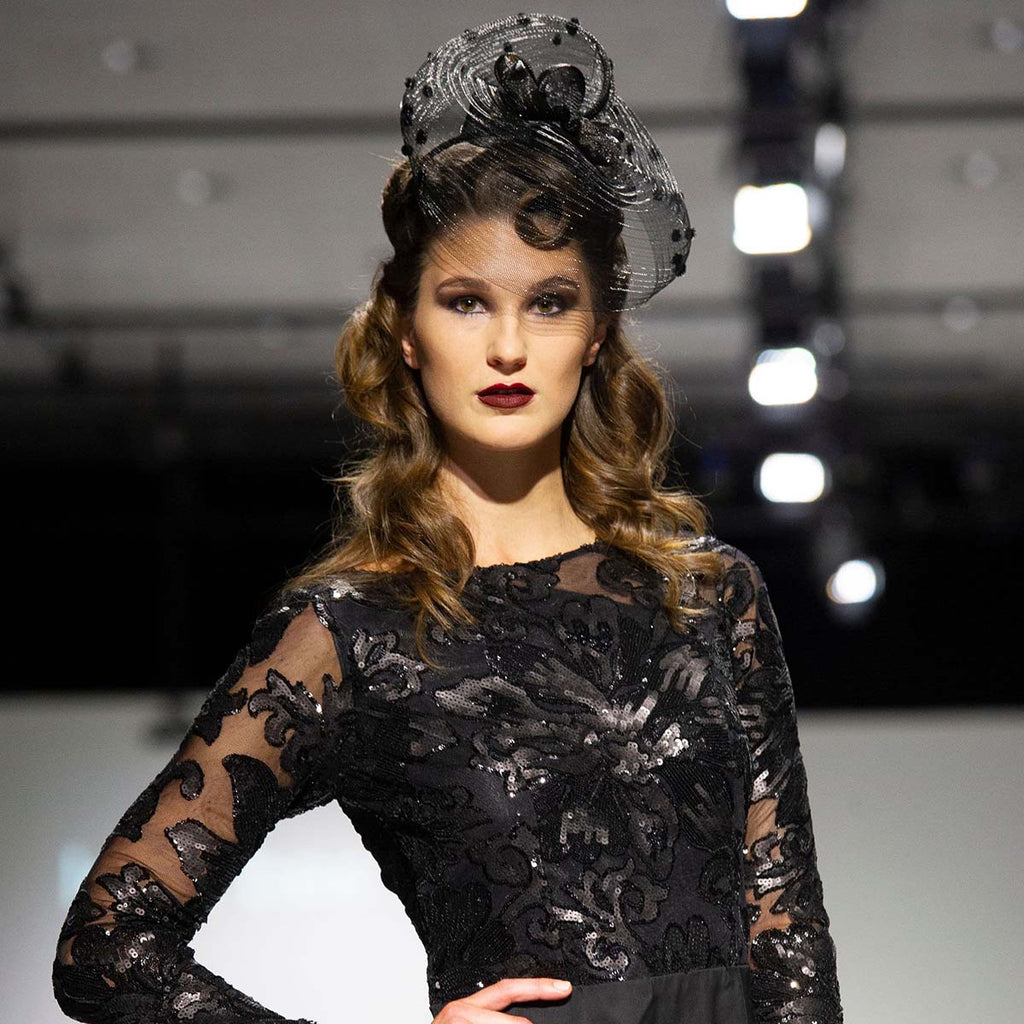 Model in black lace dress with sequins and statement headpiece walking the StyleWeek Northeast runway.