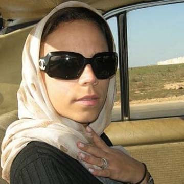 Woman wearing a headscarf and oversized sunglasses sitting in a car with countryside views in the background.