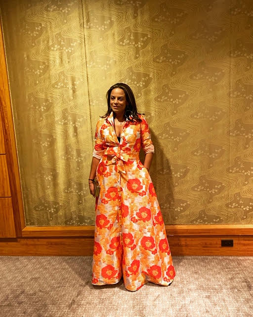 Melina Cortes-Nmili wearing a vibrant floral printed jumpsuit, recognized by WBUR as a designer to watch for her innovative fashion vision.