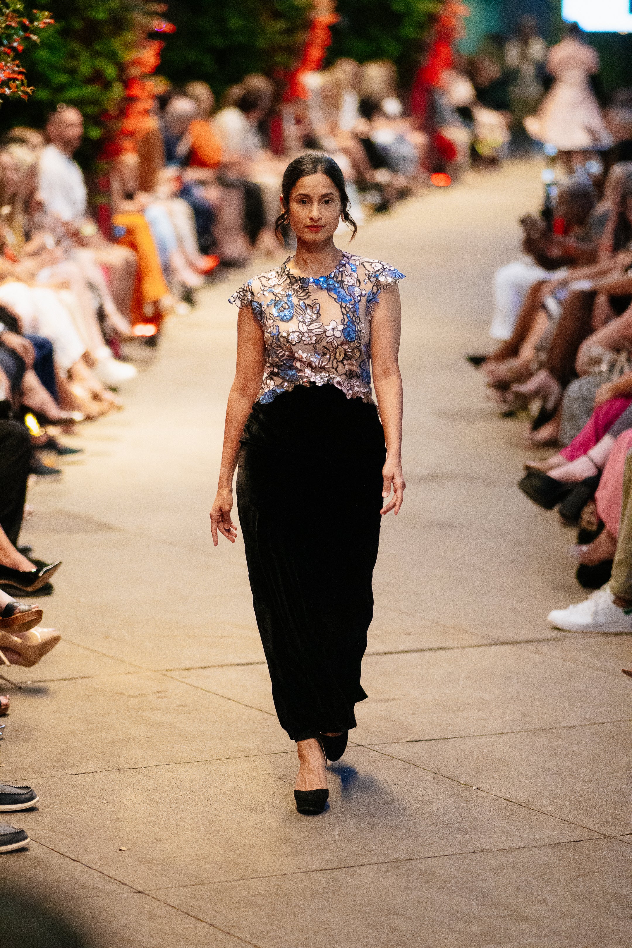 Model wearing the Lalla Bee Paris custom design gown in blush pink with black lace collar and bow details, walking the runway in an elegant ballroom setting.