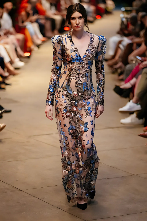 Model wearing the Olga Dress by Lalla Bee on the runway, featuring a fitted silhouette with long puffed sleeves and intricate floral embroidery.