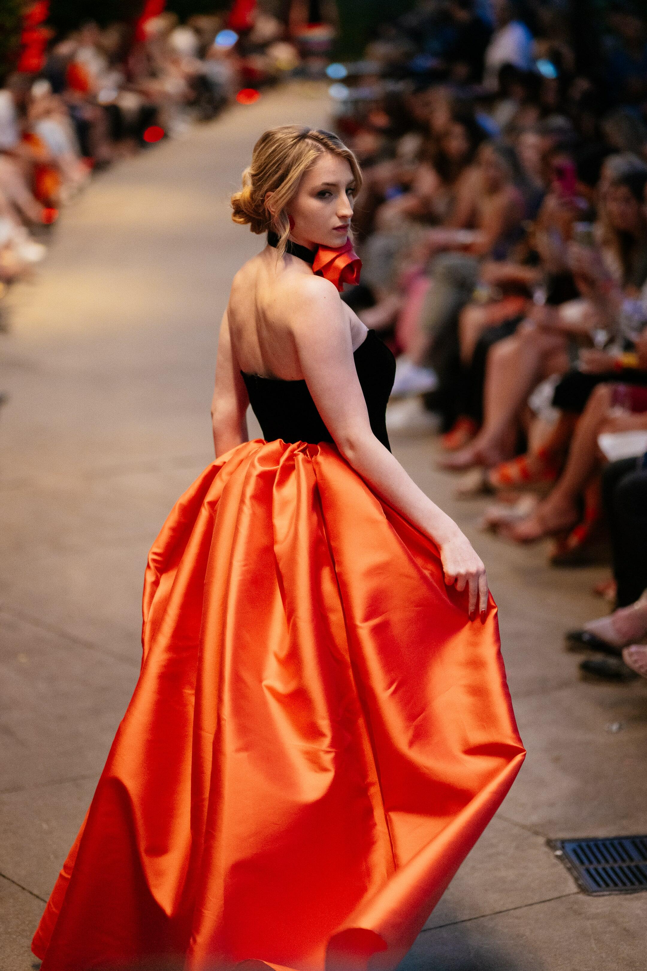 Model wearing the Chameleon Dress by Lalla Bee on the runway, styled in a bold red-orange Mikado accessory variation.
